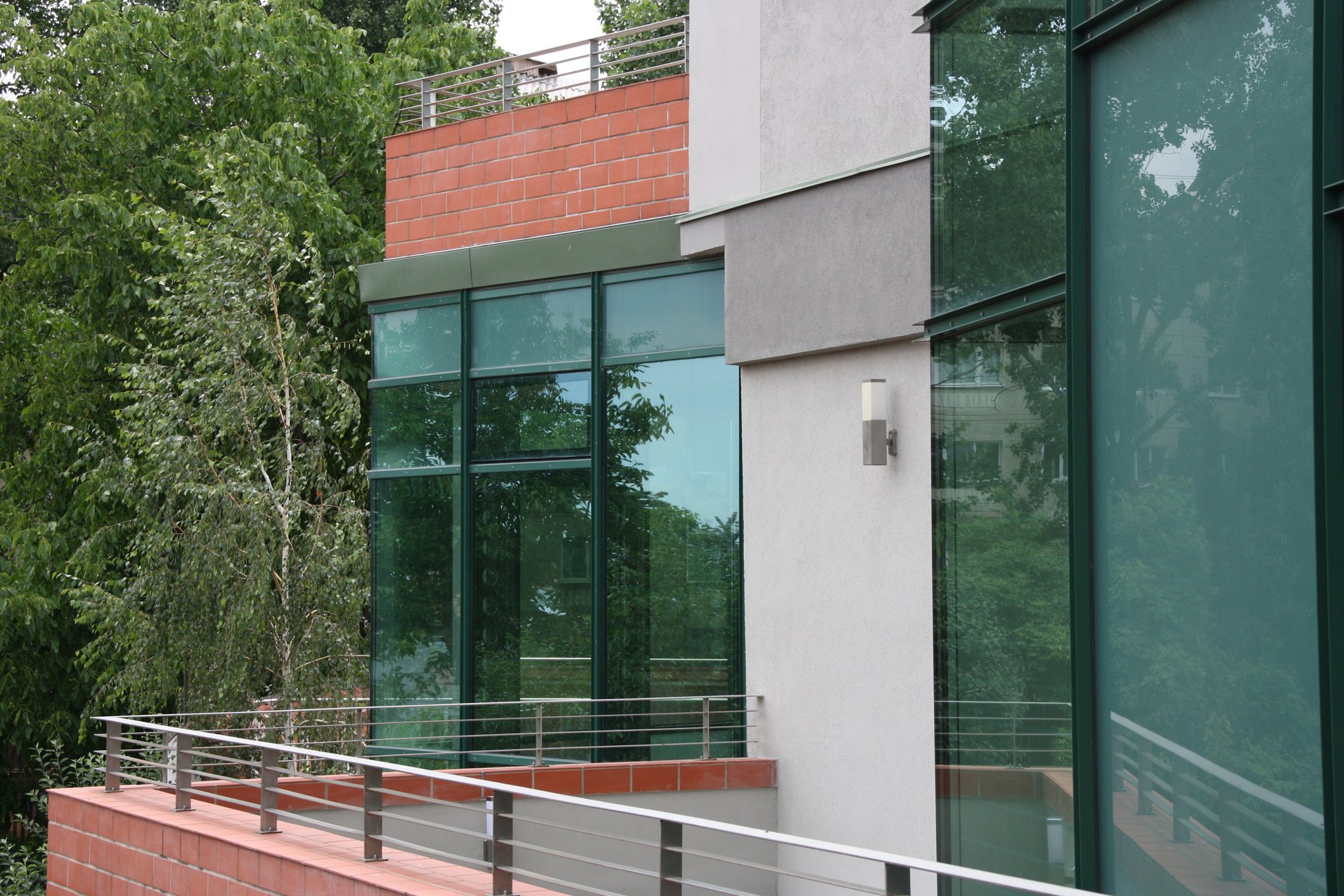 Detaliu al unei case cu geamuri mari verzi si placaj de caramida rosie pe fatada.