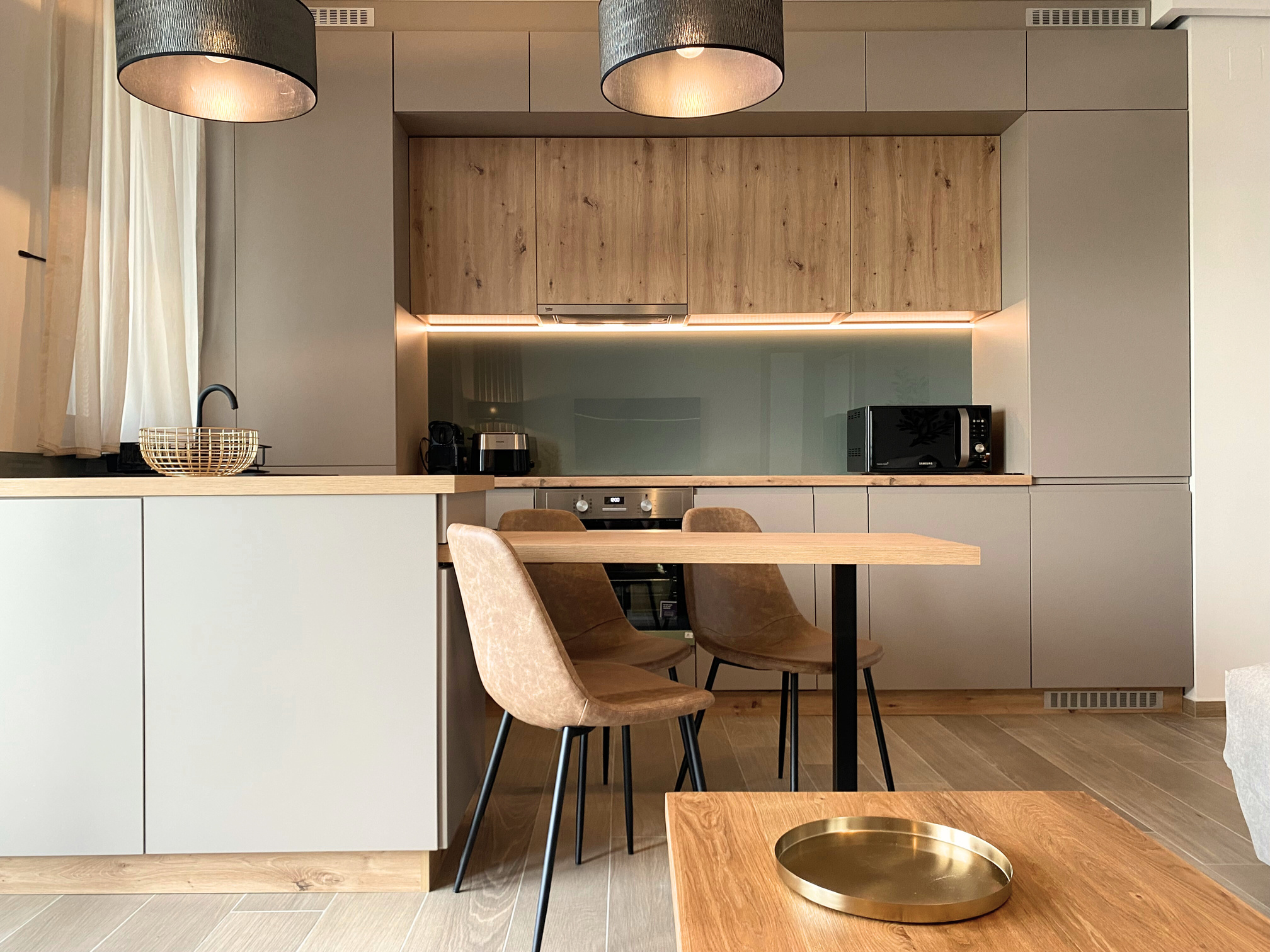 O bucatarie cu zona de dining inclus, design modern minimalist, tonuri de gri cu bej si lemn.